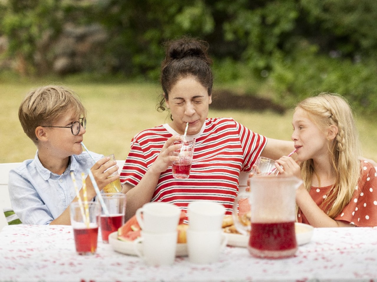 Ģimene dārzā dzer ar papīra salmiņiem limonādi.